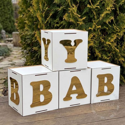white boxes for party, with gold letters spelling 'BABY' on a wooden surface with greenery in the background.