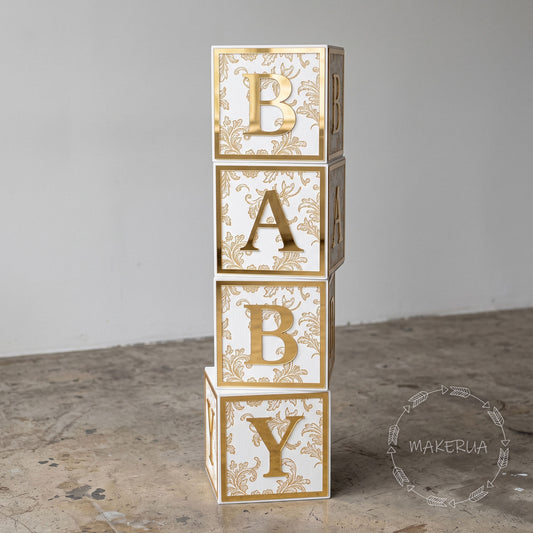 Stack of decorative baby blocks with gold lettering and floral print, on a neutral background