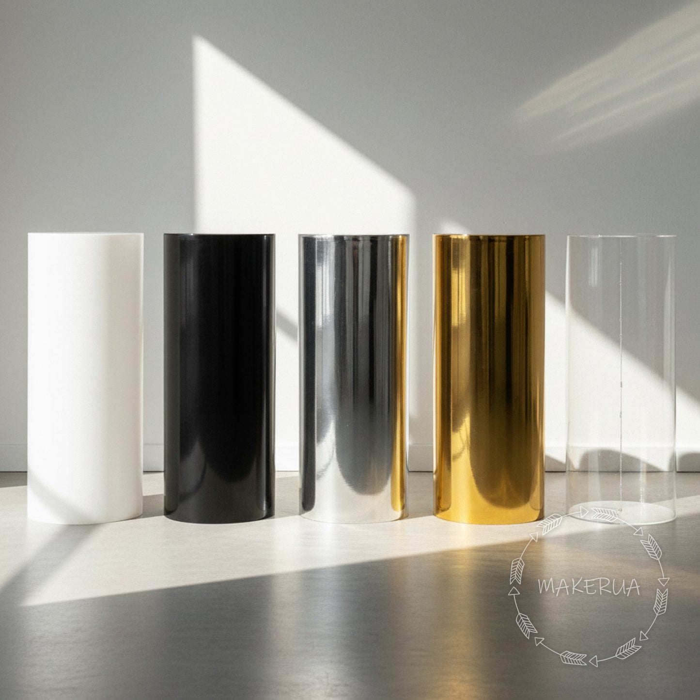 Five plinth stand column cylinder pedestal display pillar in different colors (white, black, silver, gold, clear) on a reflective surface with a blurred background by MakerUA.