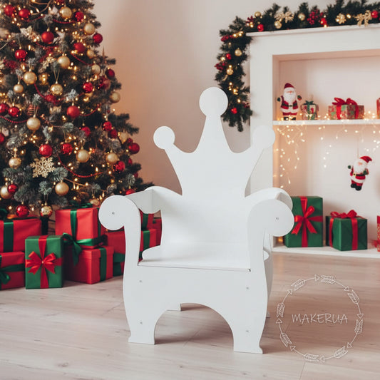 White wooden kids throne chair with a simple crown-shaped backrest. Displayed in a cozy holiday room with a Christmas tree, fireplace, and red gift boxes. Cute versatile photo prop for children's parties and studio shoots.