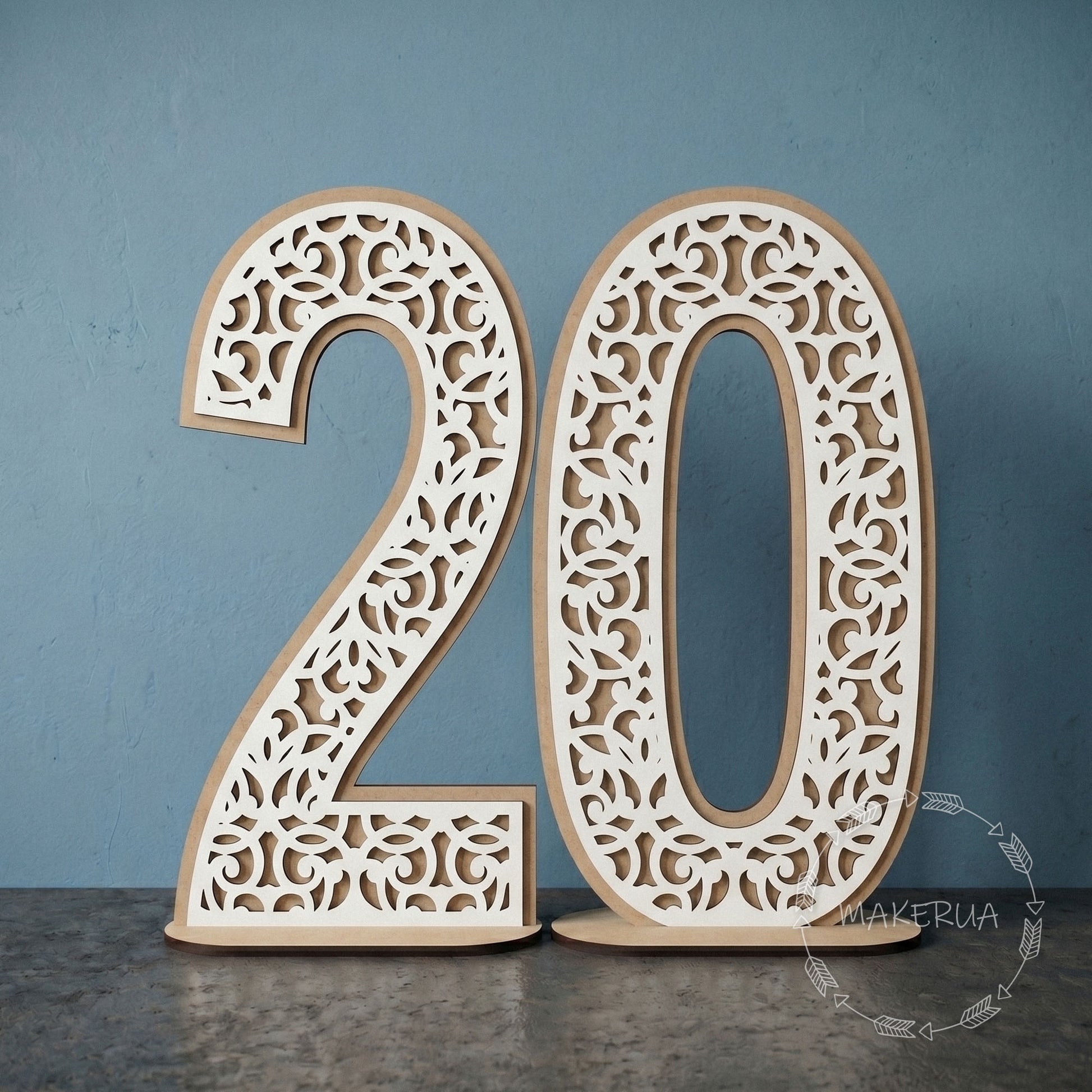 Two-layered freestanding white laminated HDF numbers 20 with intricate laser-cut lace and filigree pattern on a wooden stand against a blue studio background.